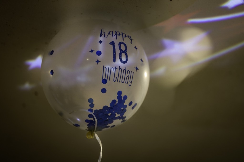 A clear balloon with blue lettering that says 'happy 18 birthday' and blue confetti inside.